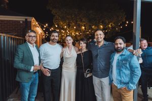 A group of people pose together at an evening outdoor gathering with string lights visible behind them.