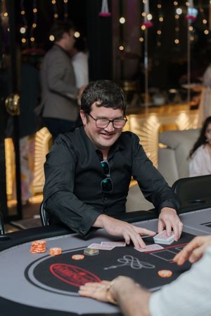 A magician performs a close-up card trick at a table with glowing lights in the background.