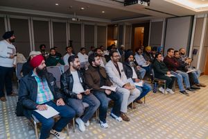 Diverse audience seated in rows at an indoor conference or seminar event, attentively listening to a presentation.