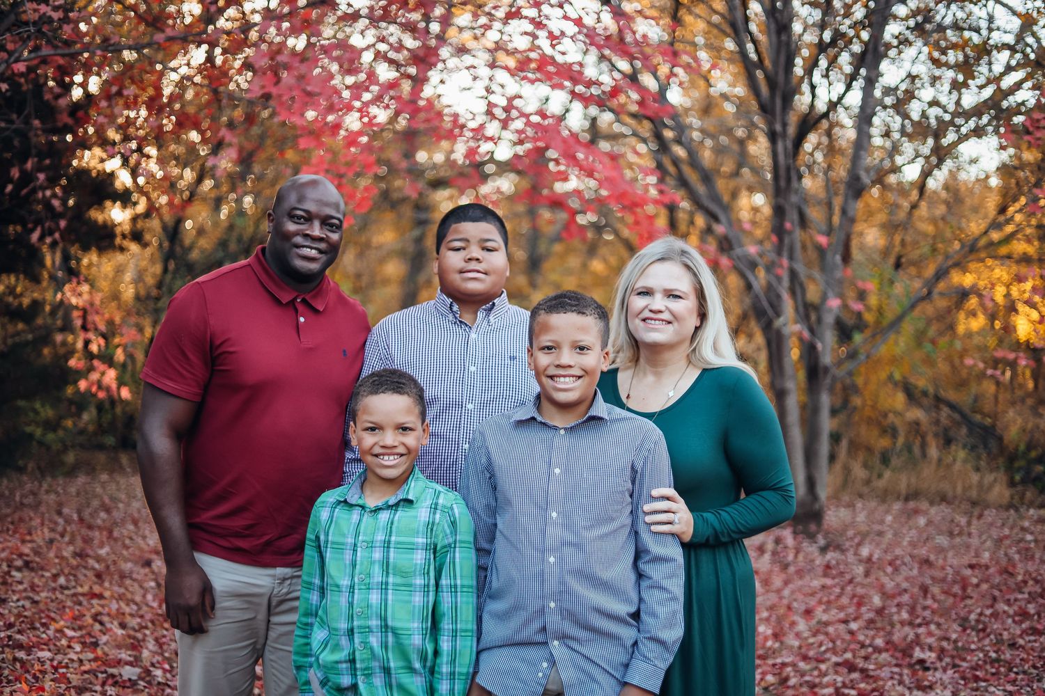 Family group poses together in autumn setting with vibrant red maple leaves and fallen foliage. Family photography