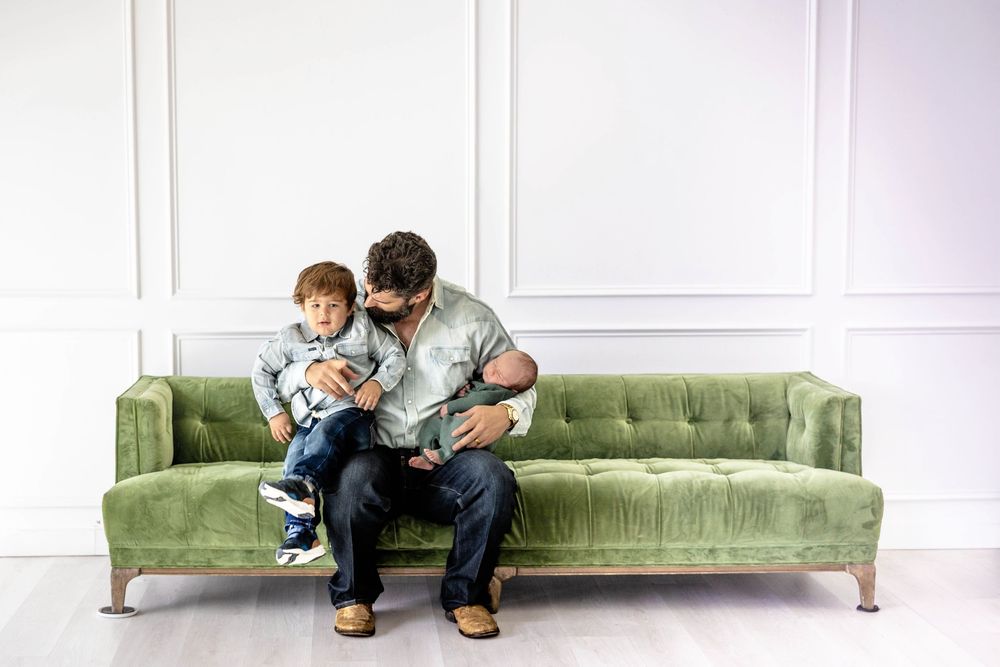 A family poses in a living room studio setting with their dog and a newborn baby.
