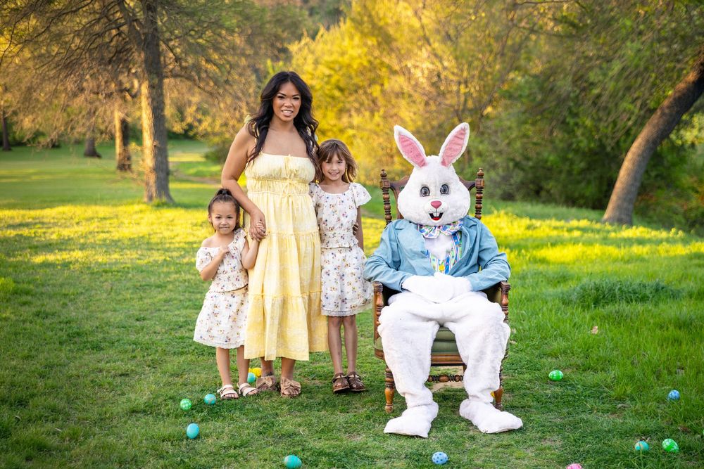 Young girls pose with their Mother in a beautiful green field with the Easter Bunny in an antique chair.