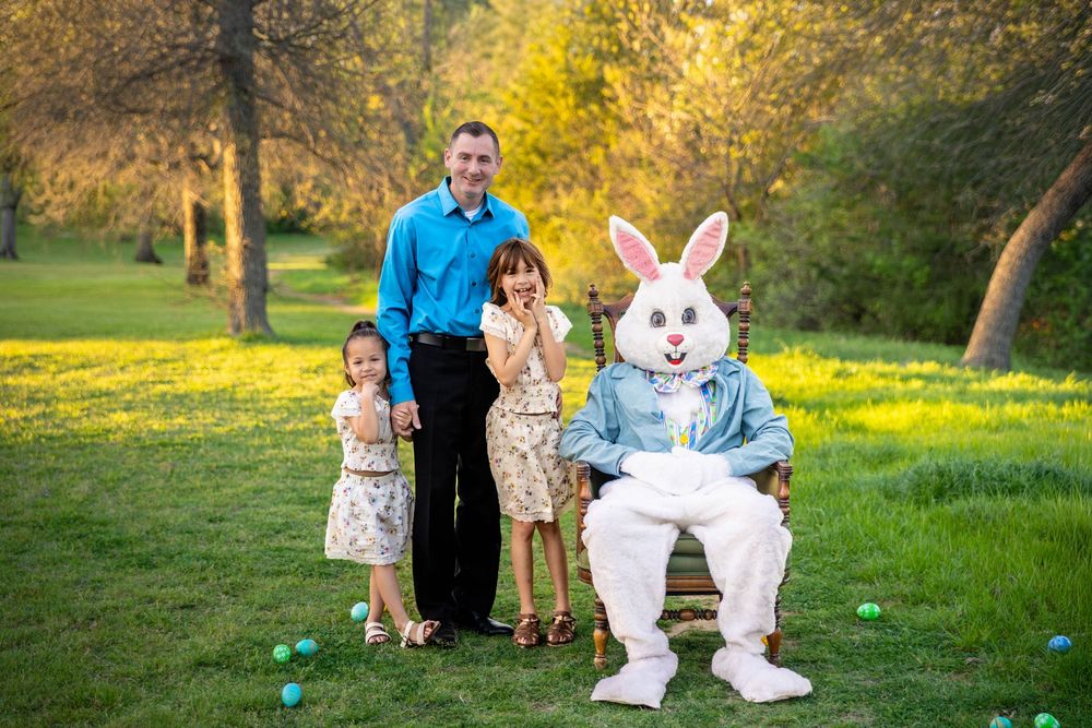 Young girls pose with their Father in a beautiful green field with the Easter Bunny in an antique chair.