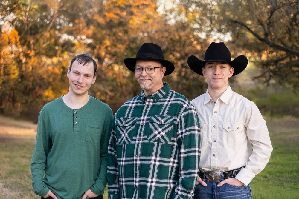 A man poses in the park with his two sons.