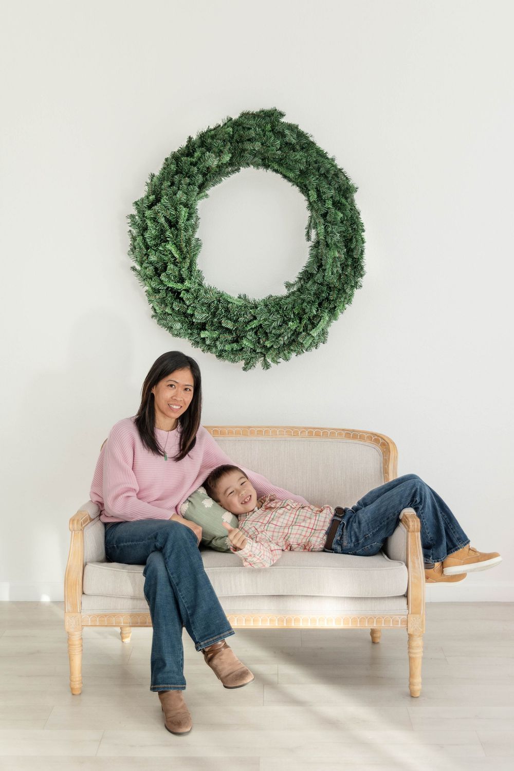 A Mother and son pose casually on a couch together in front of a wreath.