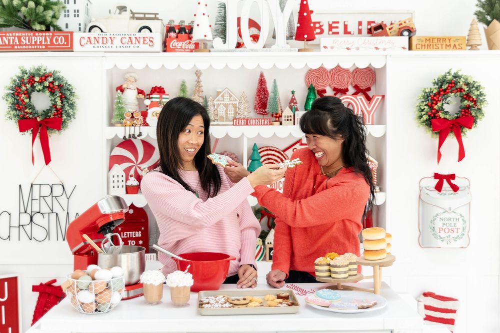 Two sisters with dark hair in a Christmas themed kitchen feeding each other cupcakes.