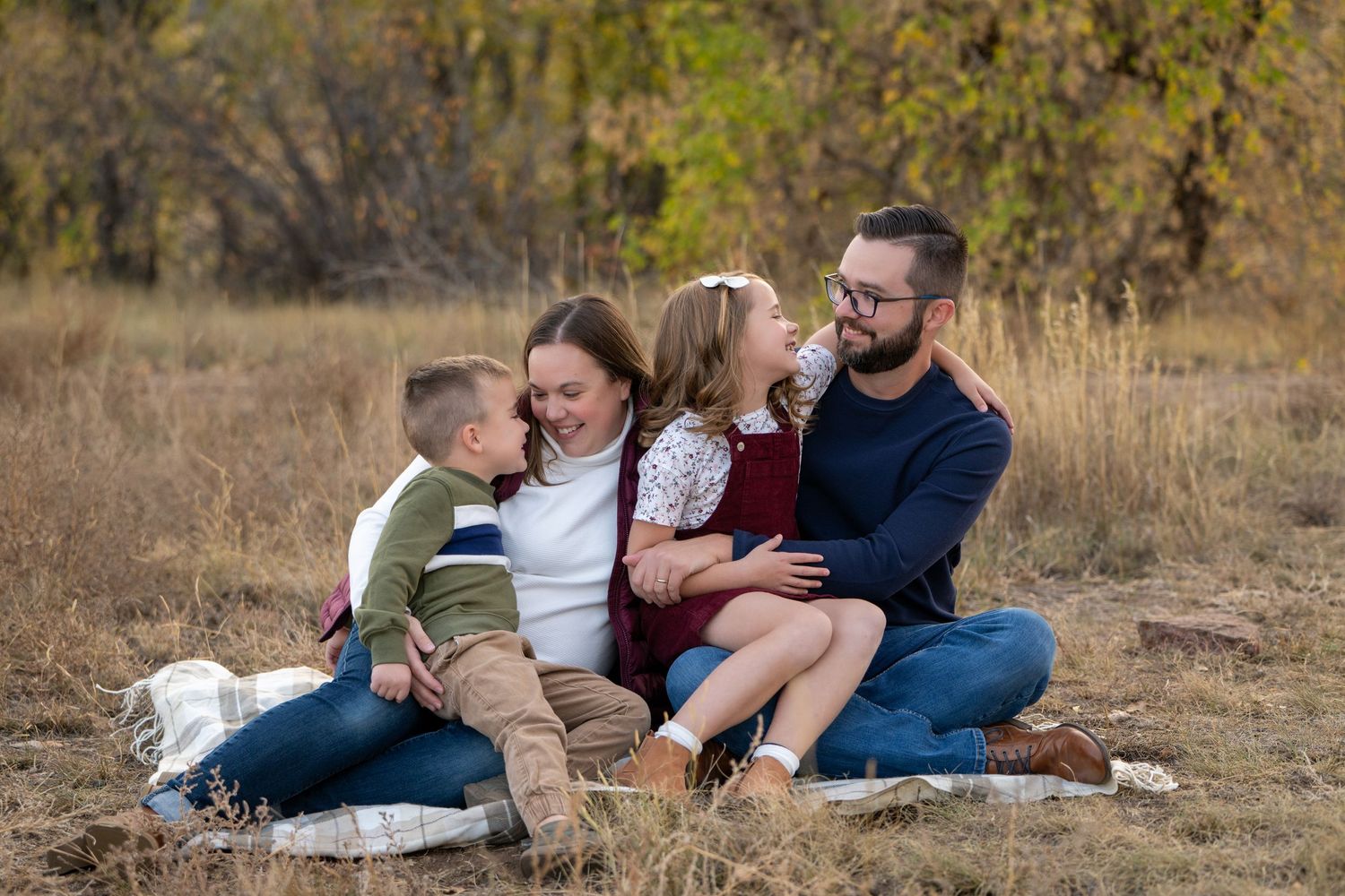 Family of four relaxing together on blanket in autumn field.