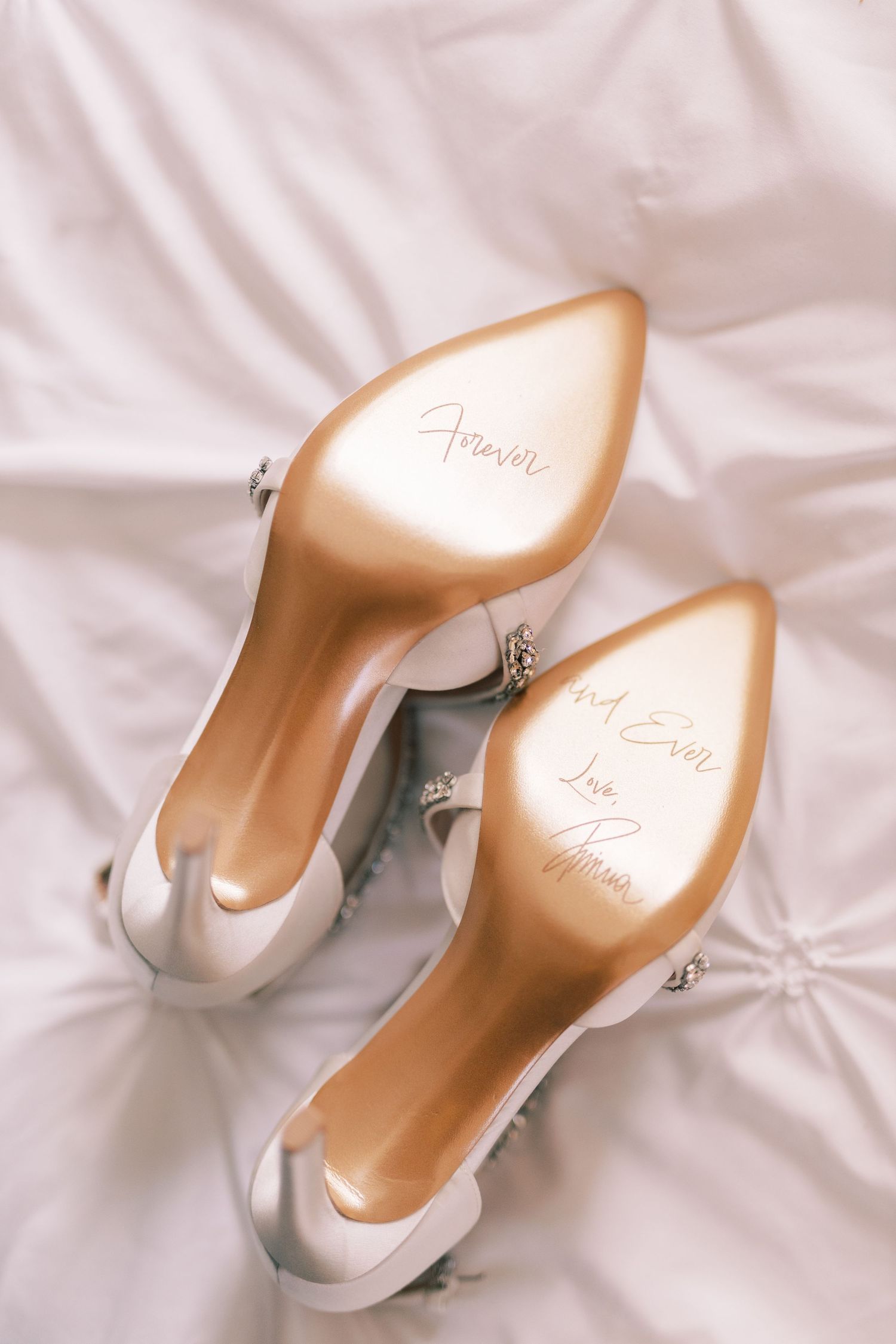 White bridal heels with personalized handwritten forever message on gold soles on white fabric.