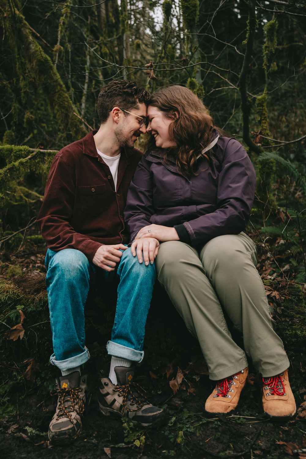 Couple is sitting in the forest their forheads pressed together.