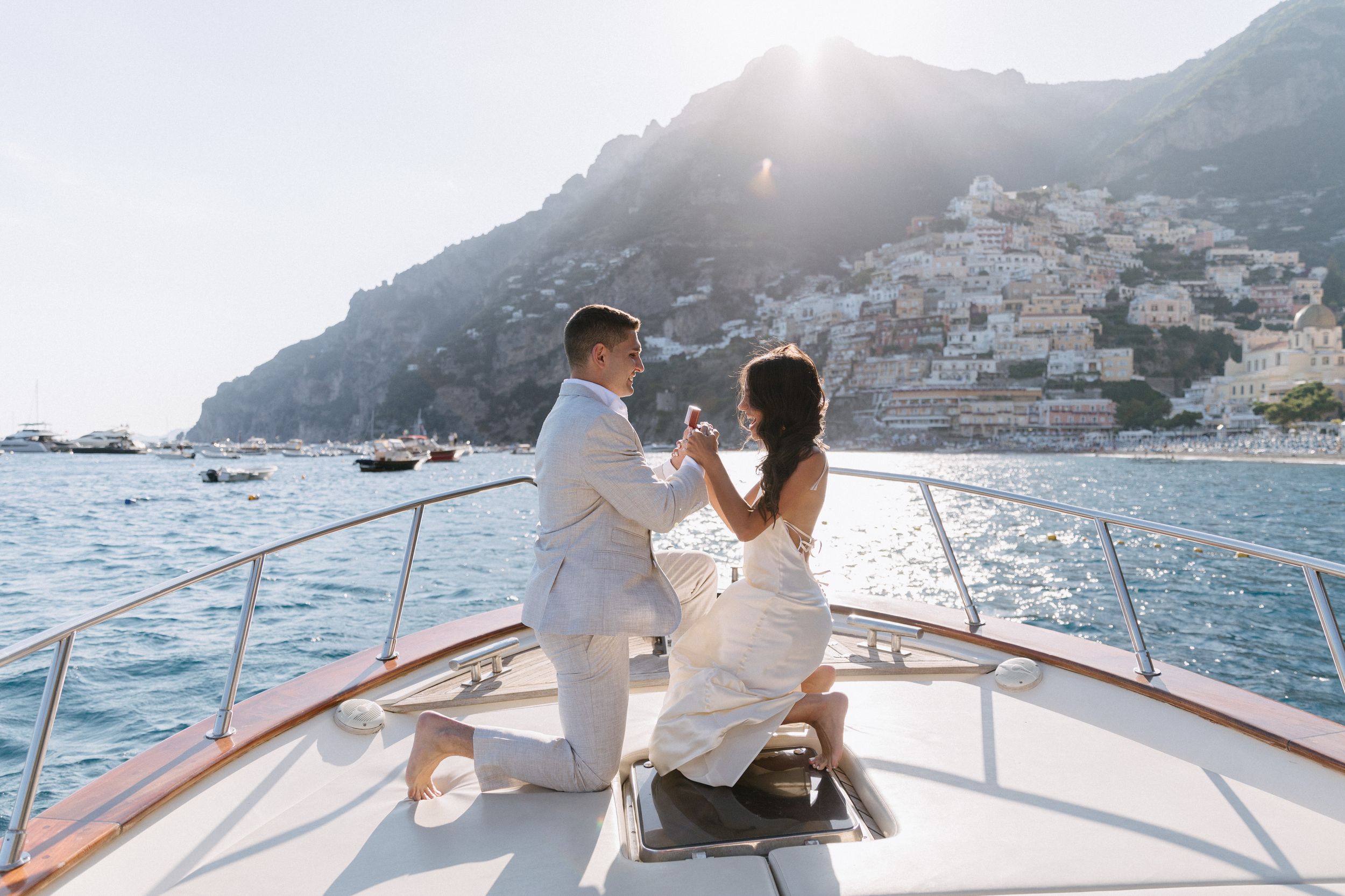 Couple celebrating engagement on luxury yacht bow with stunning Positano cliffside backdrop on sunny day.
