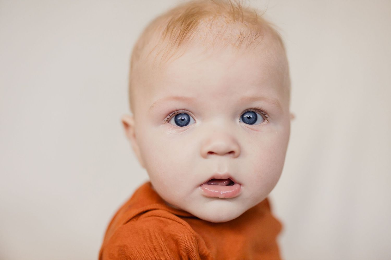 Close-up of a baby in orange clothing with bright blue eyes looking directly at camera.