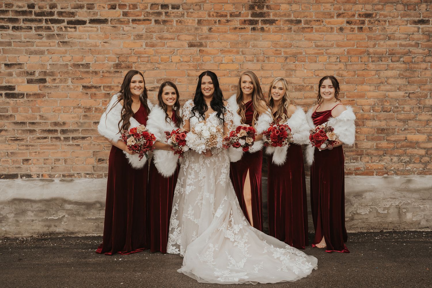 Wedding party poses against a rustic brick wall in southern Michigan with bridesmaids in burgundy dresses.