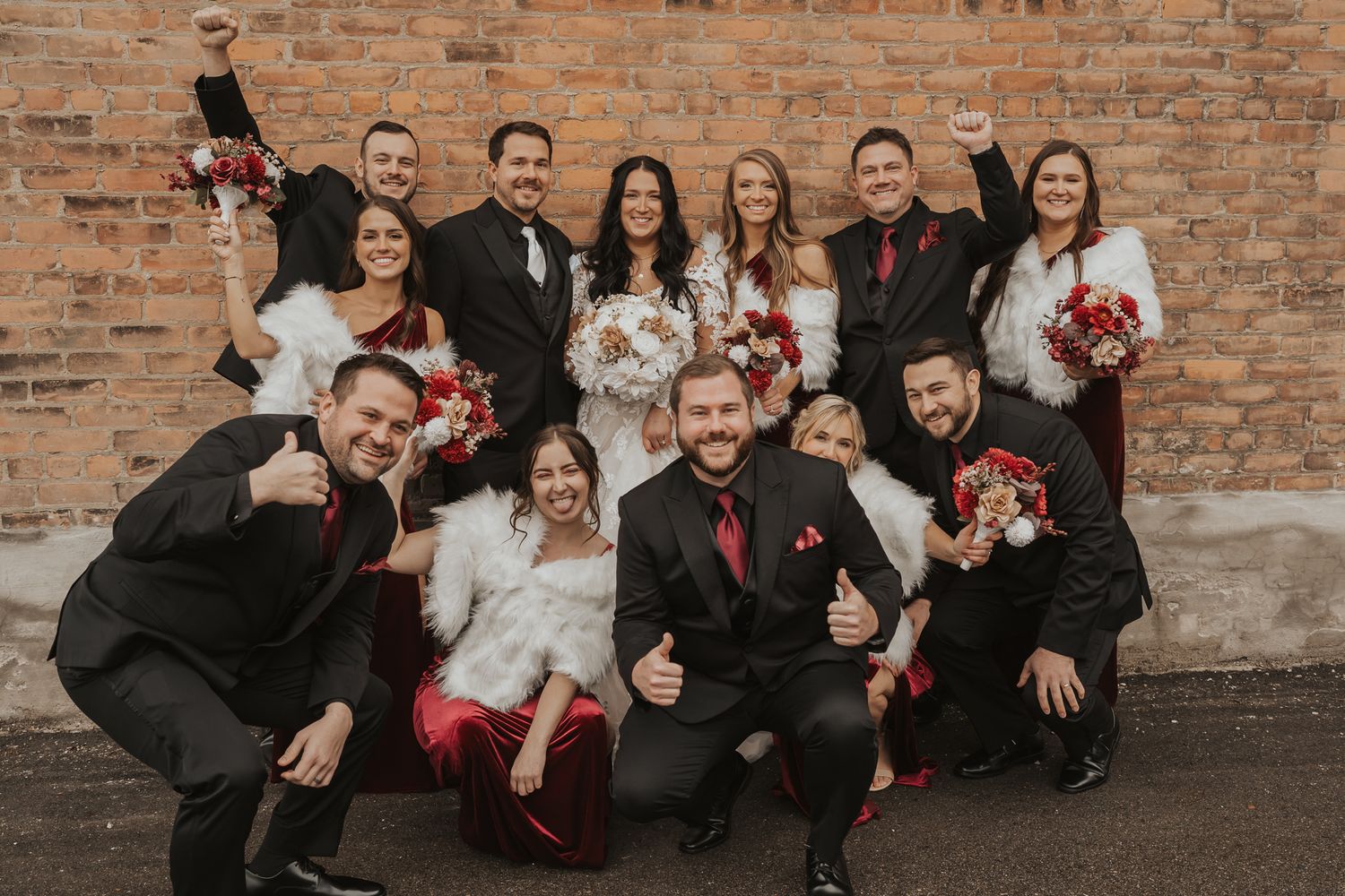 Wedding party members strike fun poses against brick wall.