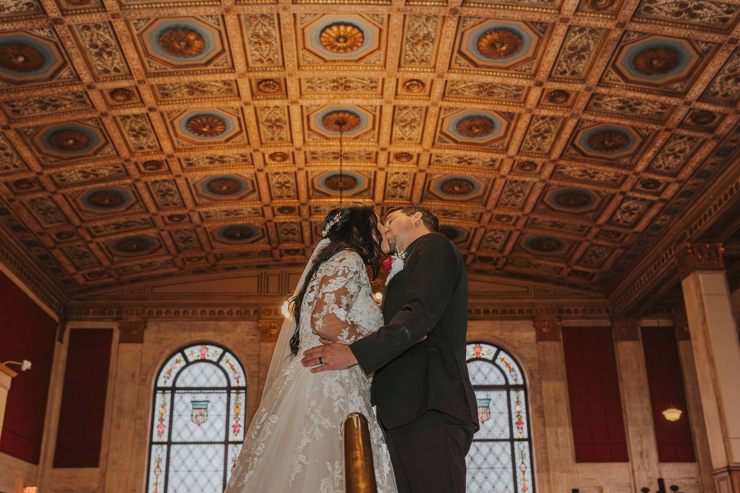Elegant wedding ceremony under ornate gold ceiling with arched windows.