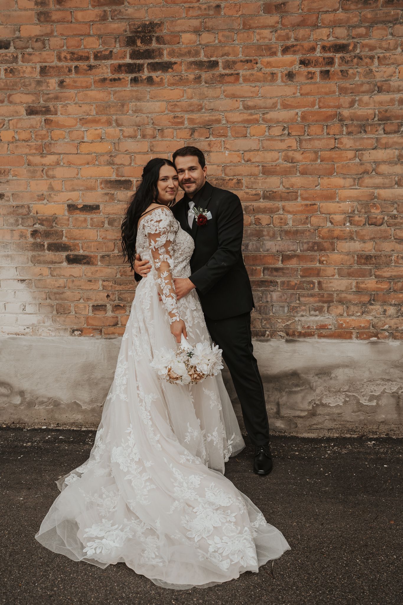 Romantic wedding portraits showcase lace dress details against rustic brick wall in downtown Jackson MI.