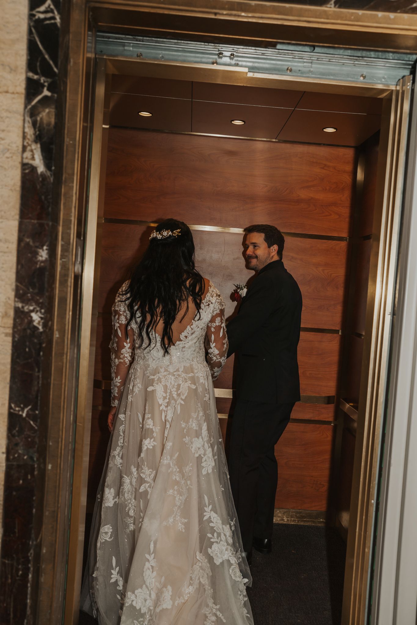 A couple in wedding attire standing in a wood-paneled elevator in Jackson MI.