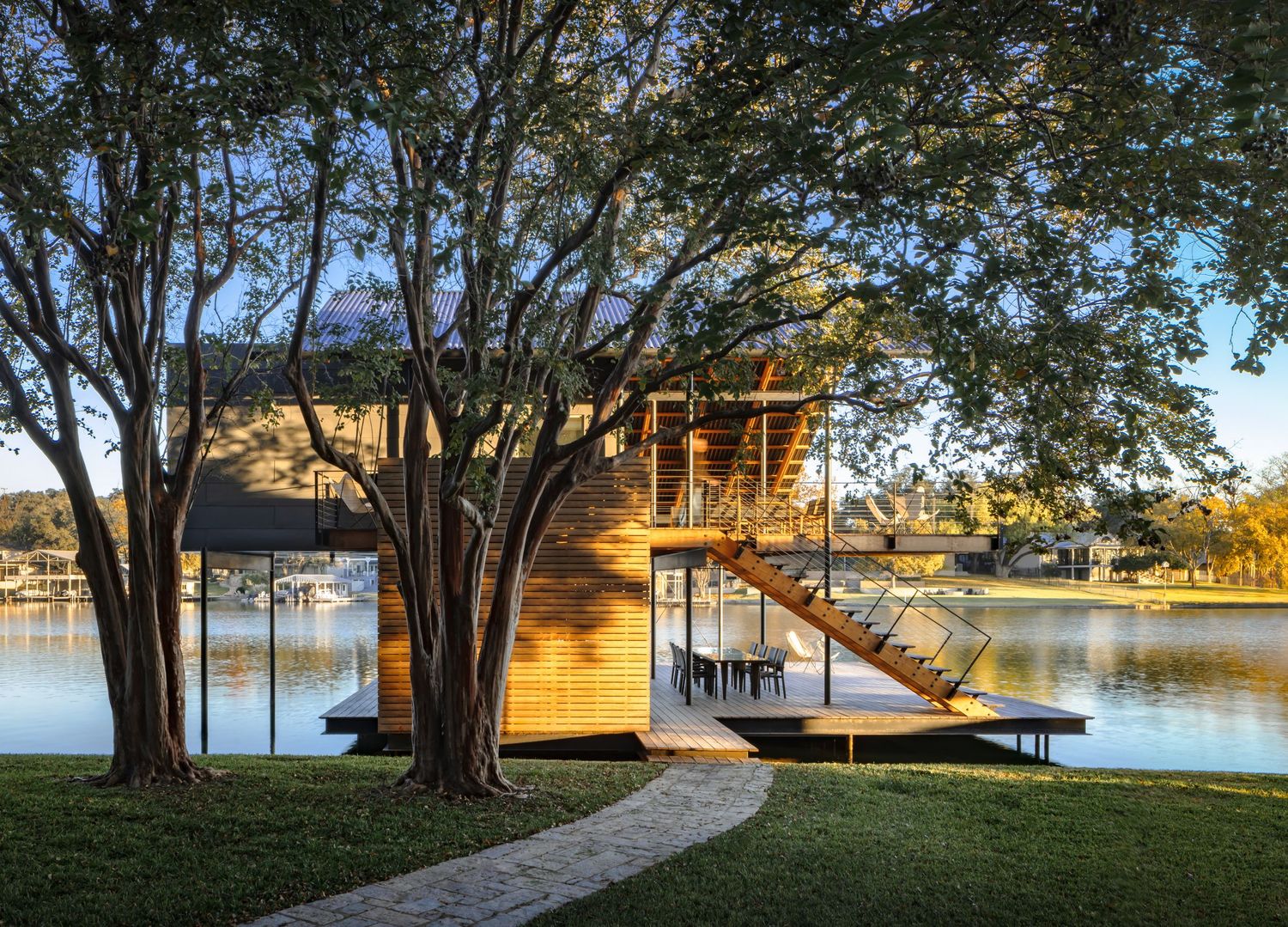 Stunning lakeside treehouse with wooden exterior, glass walls, and staircase surrounded by mature trees at golden hour.