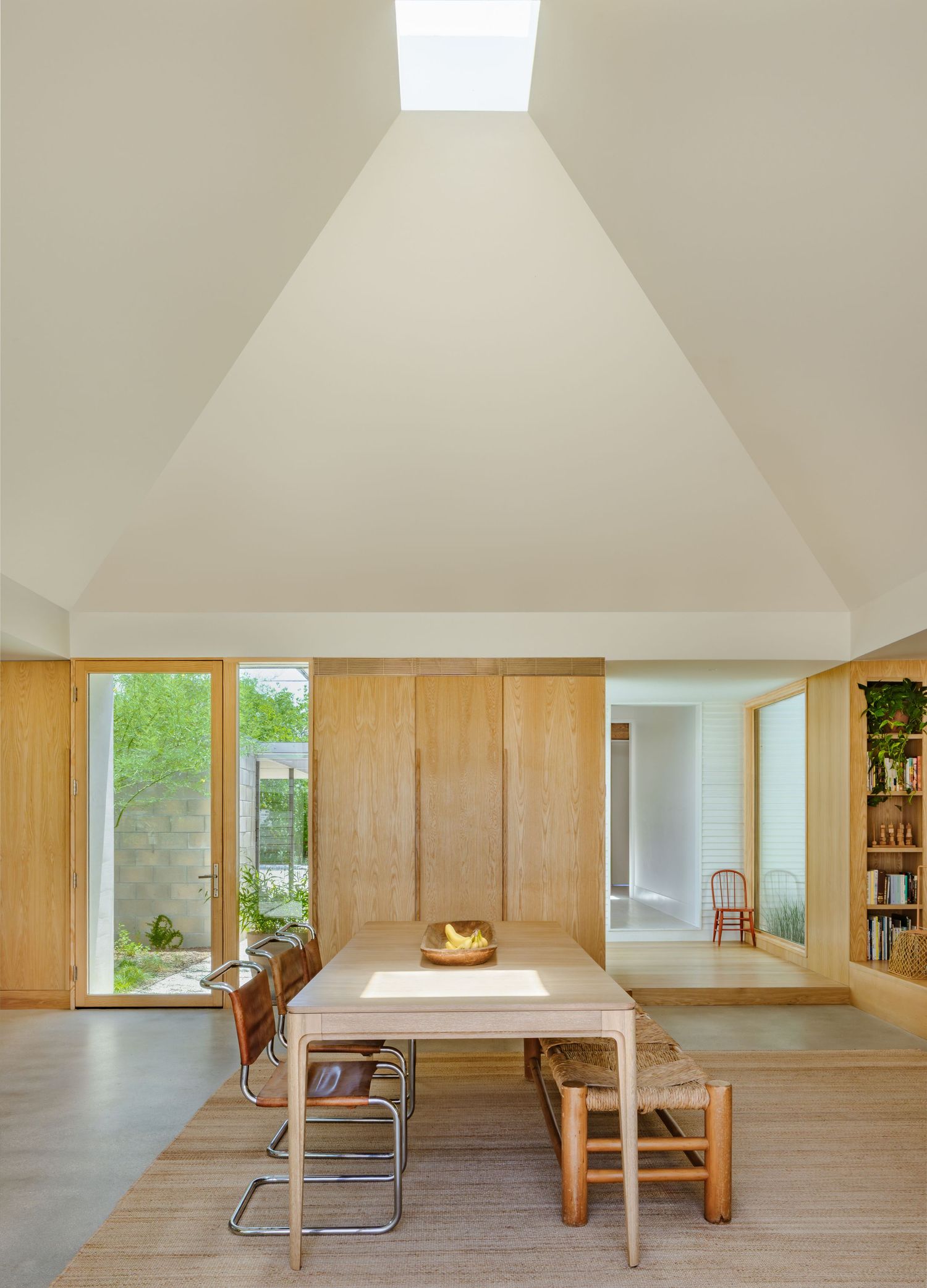 Modern minimalist living space with vaulted ceilings, natural light, and wooden furniture creates an airy atmosphere.