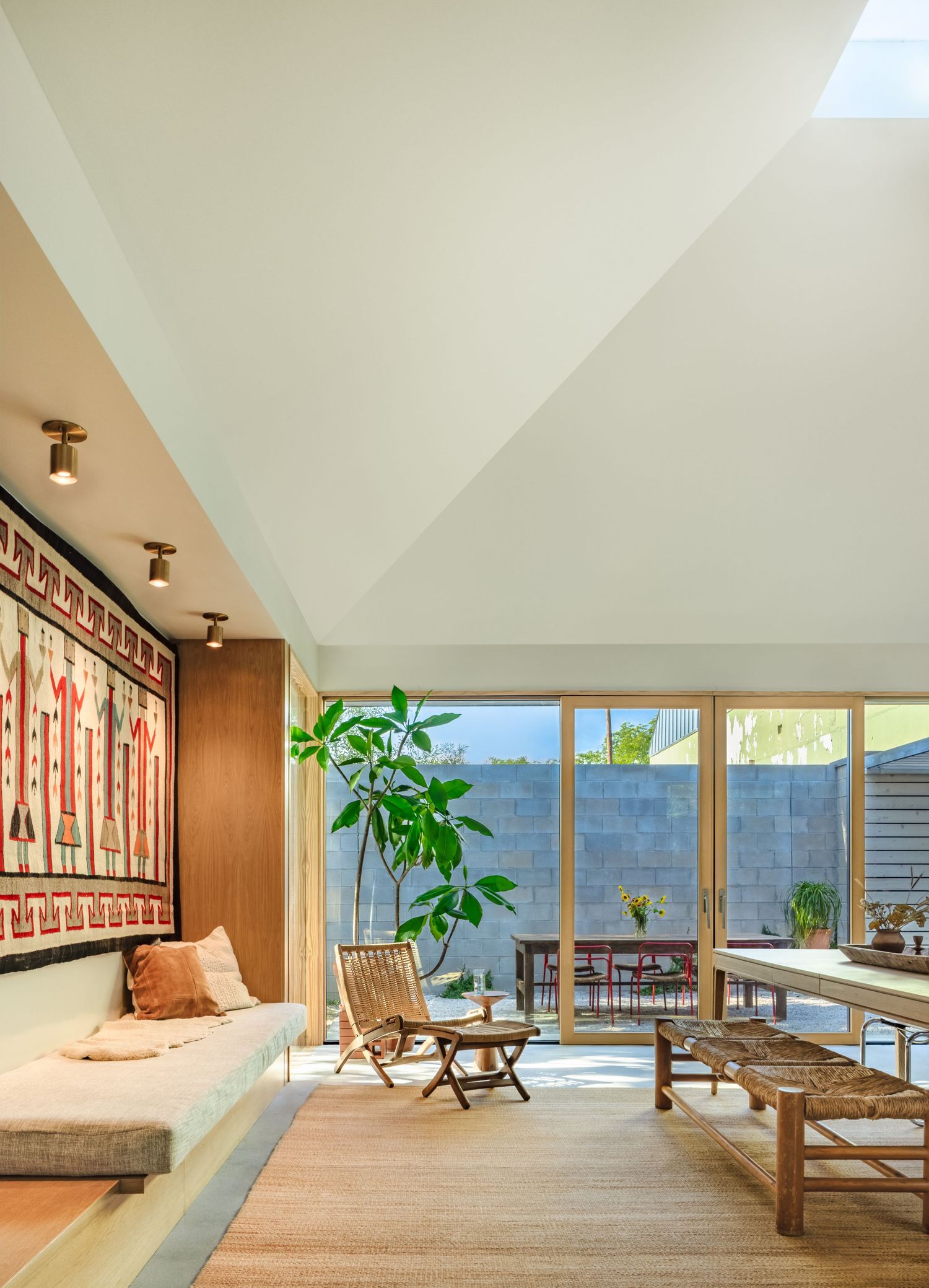 Spacious living area with floor-to-ceiling windows, tropical plants, and mid-century modern furniture.
