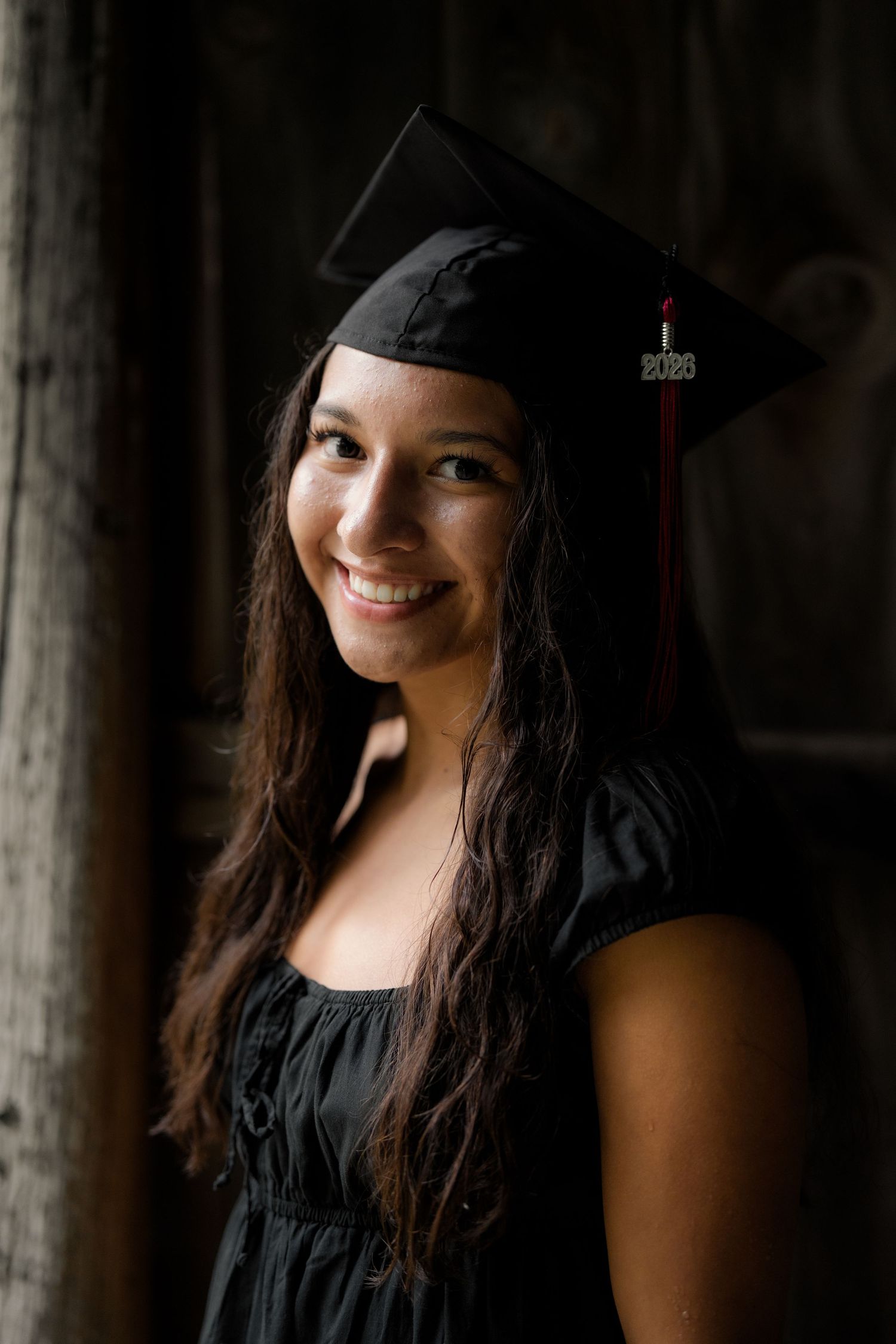 Smiling young woman wearing black graduation cap and gown for class of 2026 portrait photo.