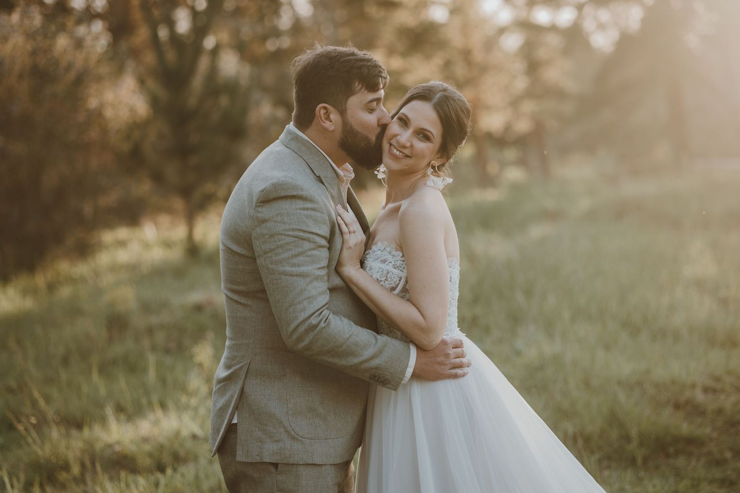 A happy couple enjoying their wedding day on a wooden bridge by a pond at sunset.