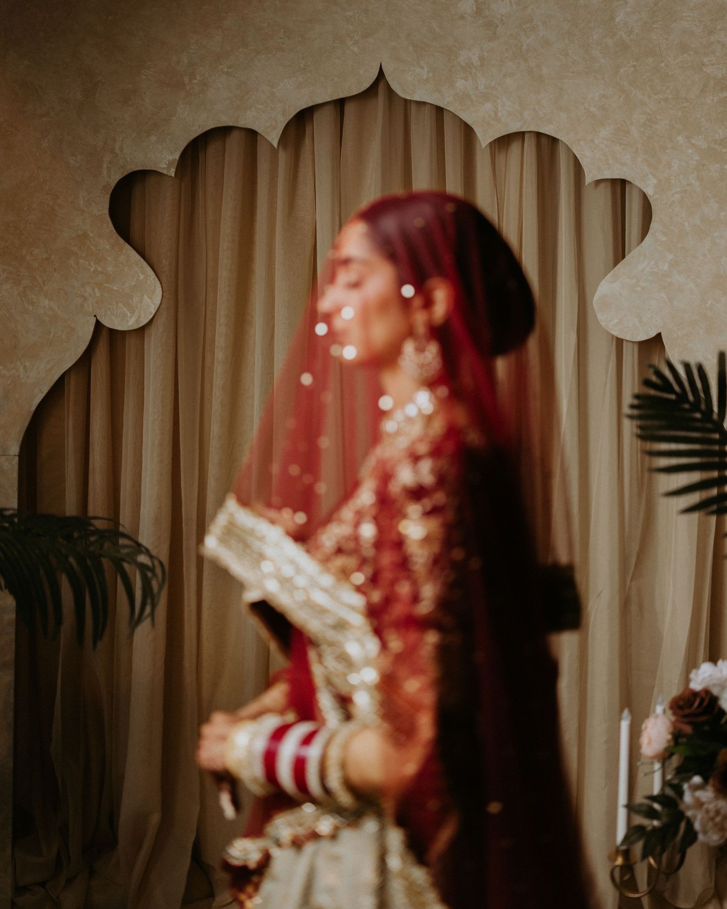 Artistic portrait in red tones showing intricate jewelry details and traditional bridal attire.