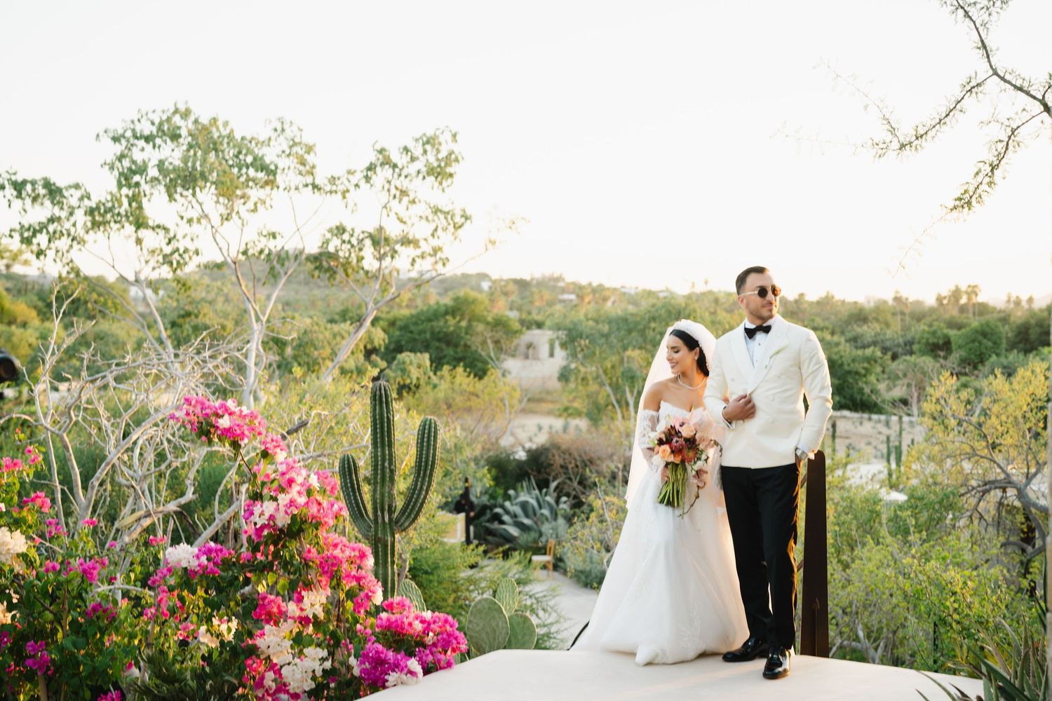 Desert wedding ceremony with pink bougainvillea flowers and cacti in natural landscape.