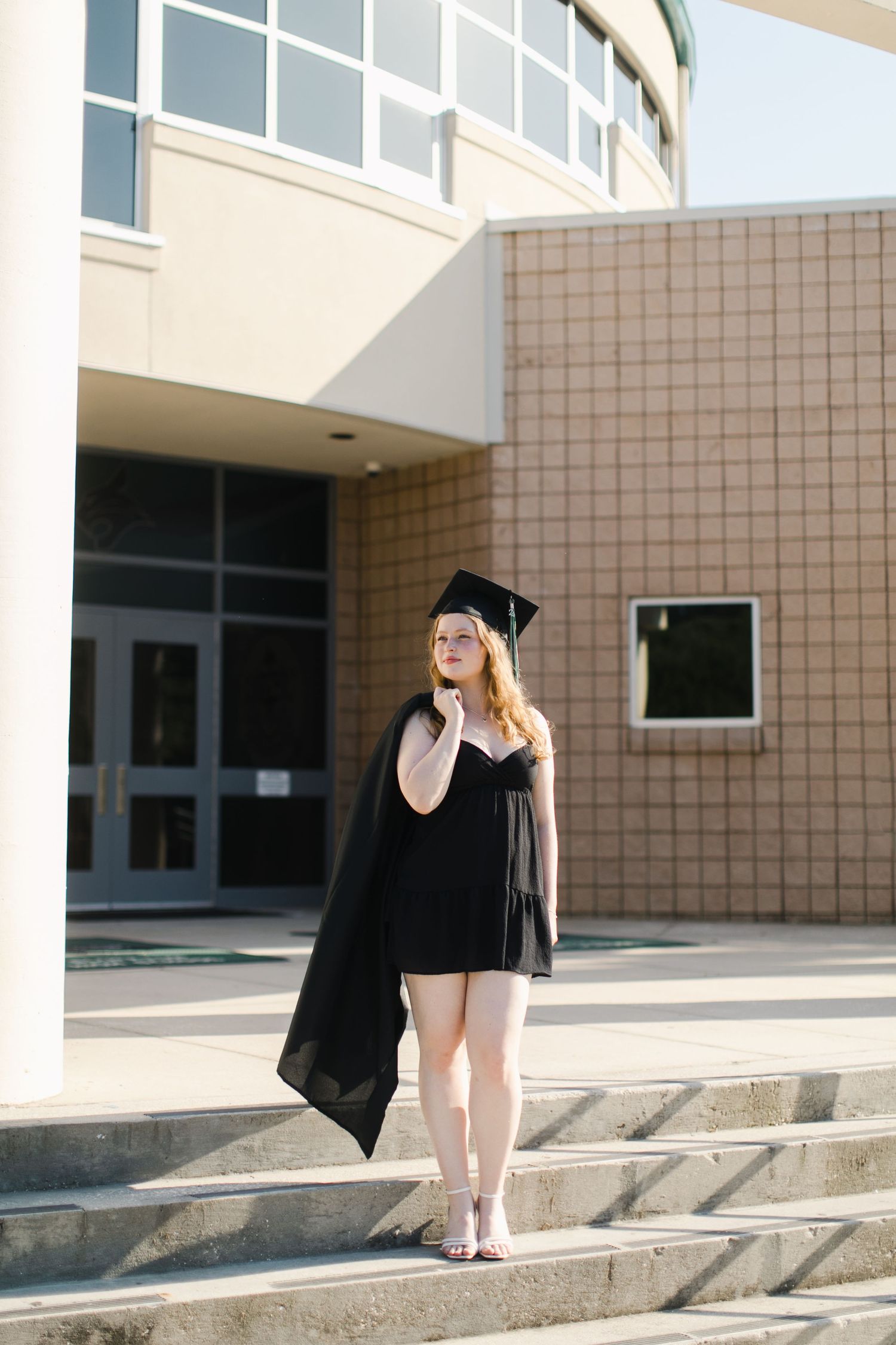 A girl in graduation attire walks down concrete steps outside a modern building in a series of progressive shots for Bluffton senior session