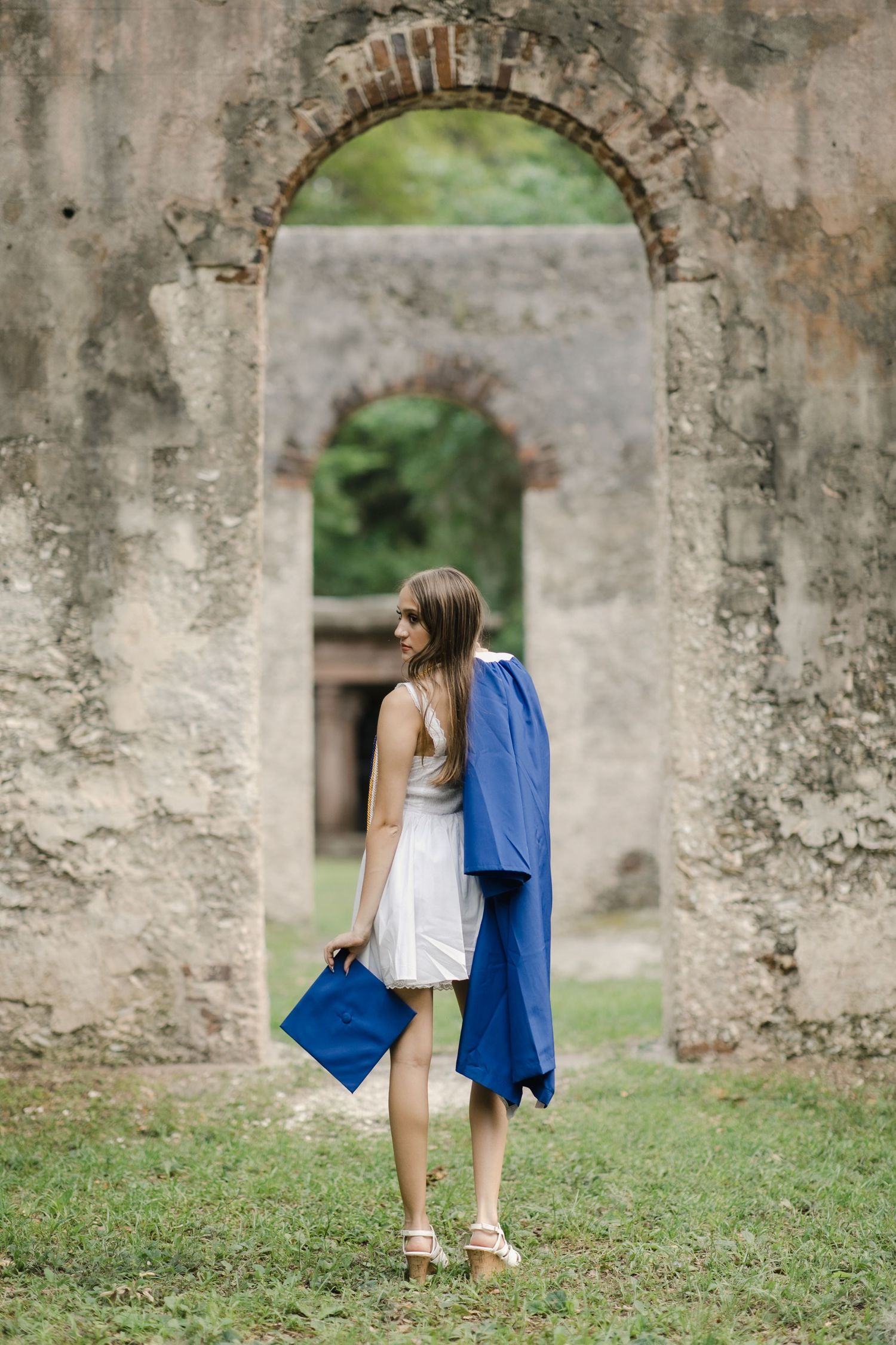 A sequence of senior session photos showing someone in a white dress and blue towel walking through stone archways in Saint Helena, SC.