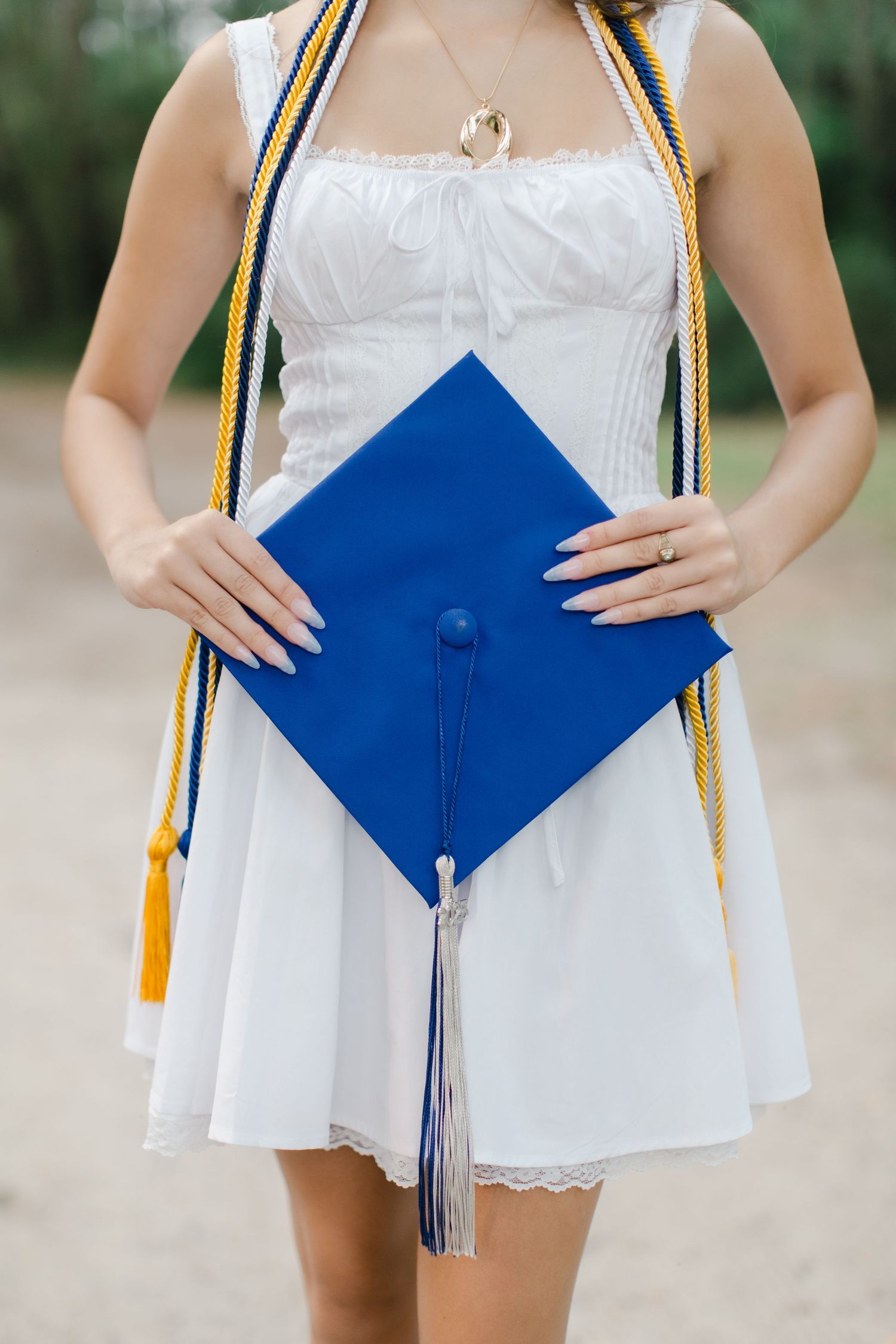 A series of graduation photos showing a blue mortarboard cap held against a white dress with gold and blue honor cords for Bluffton senior.