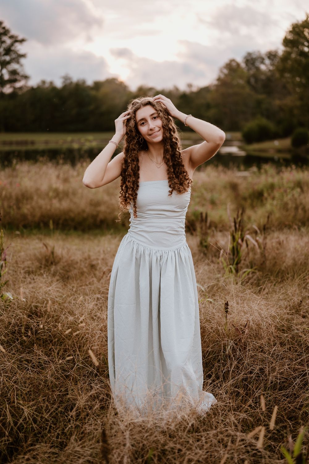 A person in a flowing white dress poses gracefully in a golden field at sunset.