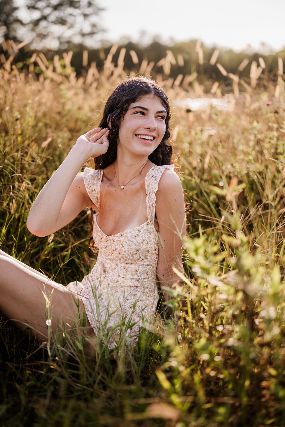A woman in a cream lace dress lies in a sun-dappled meadow during golden hour.