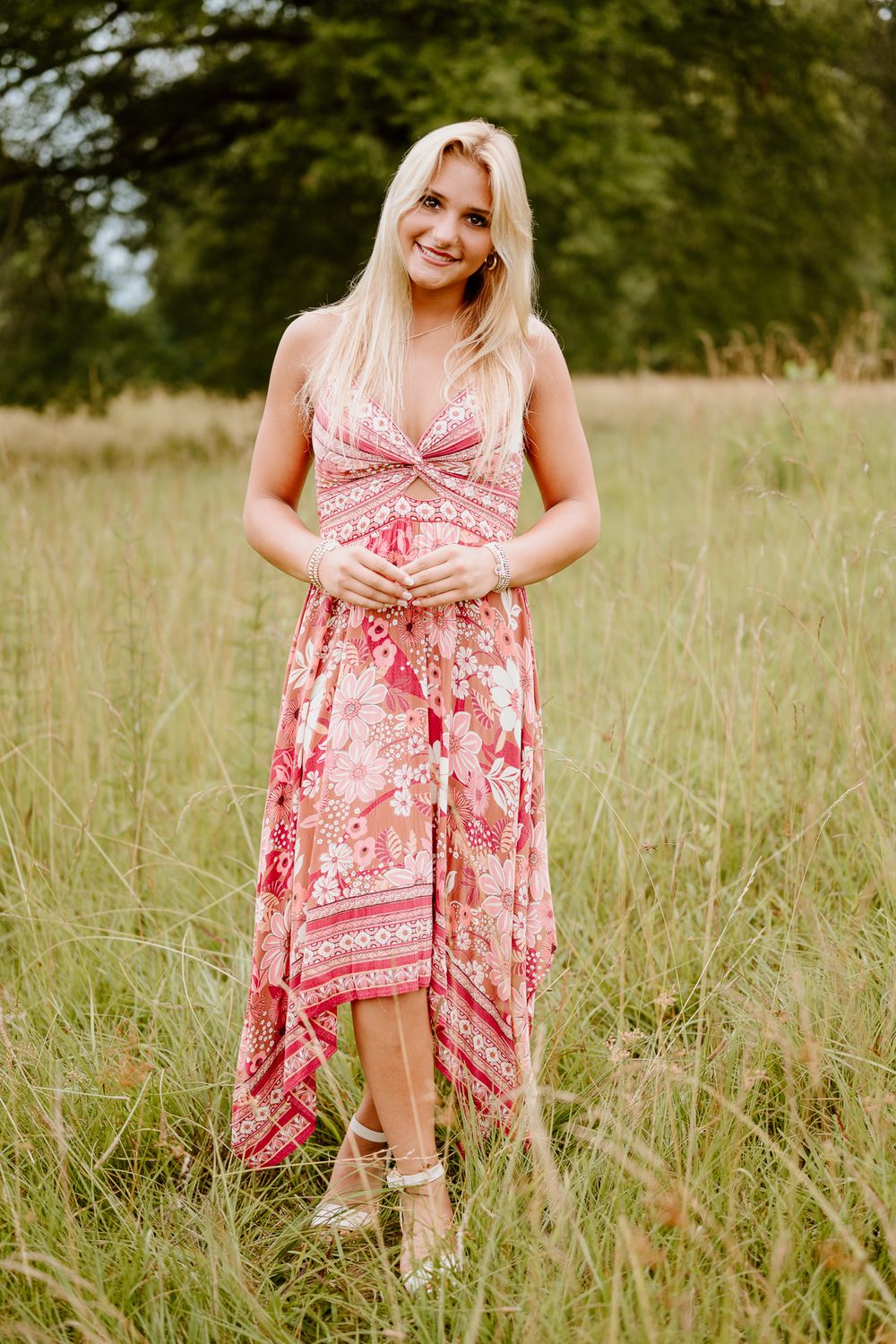 Someone poses in a flowing pink floral maxi dress with handkerchief hem standing in a summer meadow of tall grass.