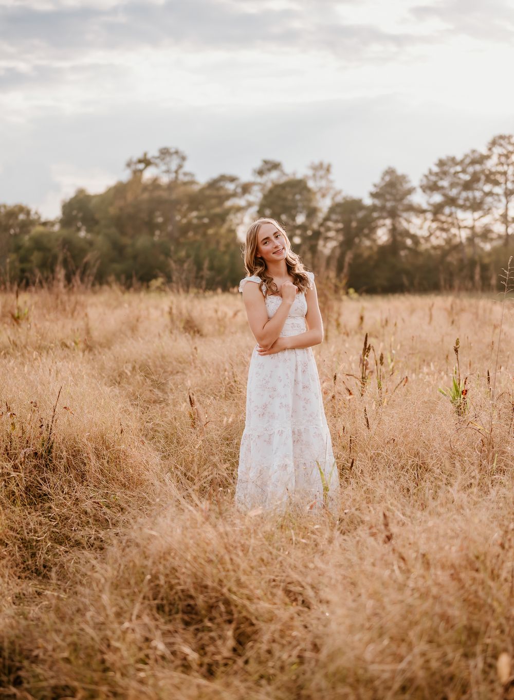 A white dress flows gracefully through golden grass in a dreamy outdoor field at sunset.