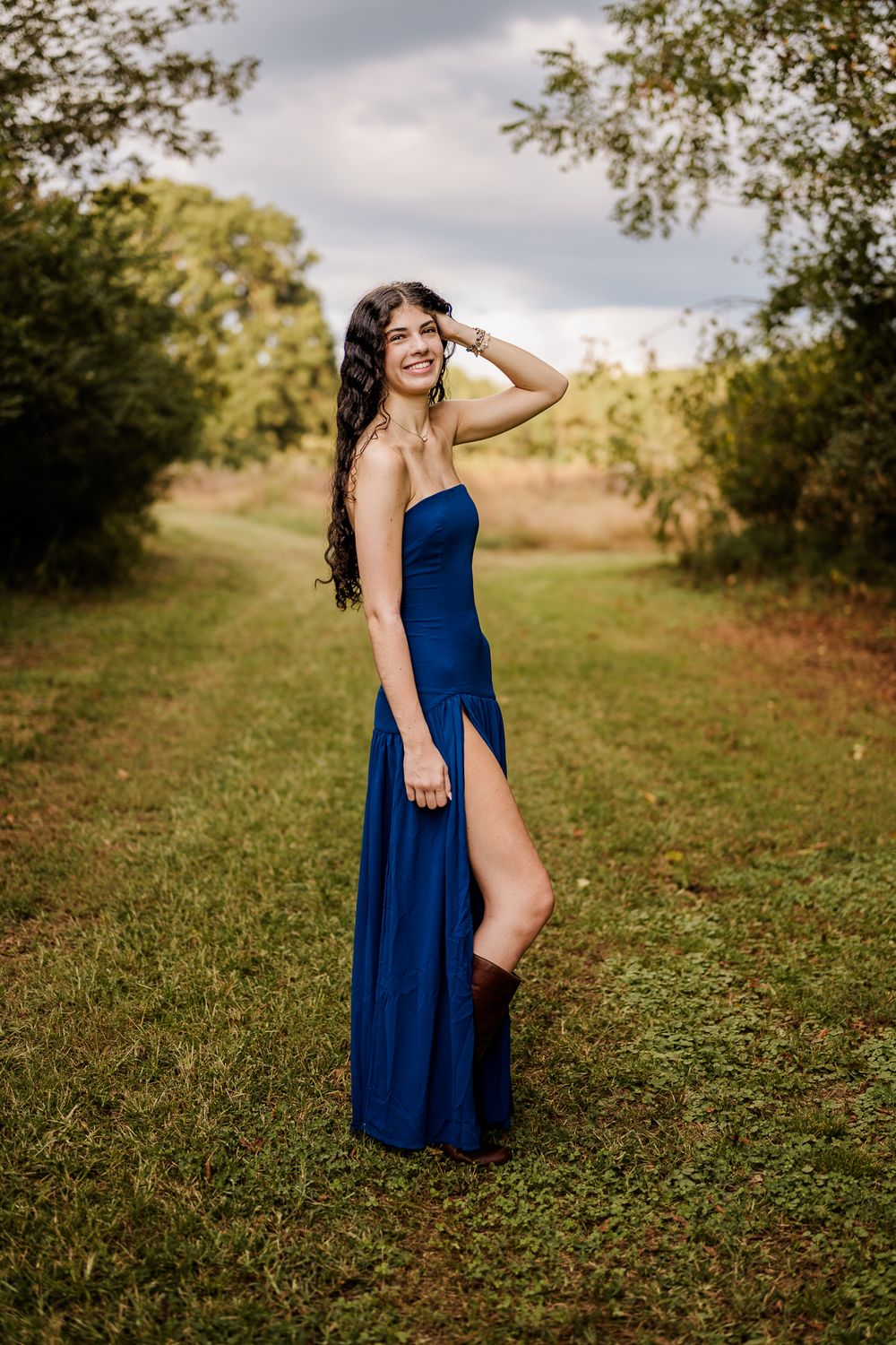 A woman in a flowing navy blue dress poses gracefully in a sunlit meadow during golden hour.