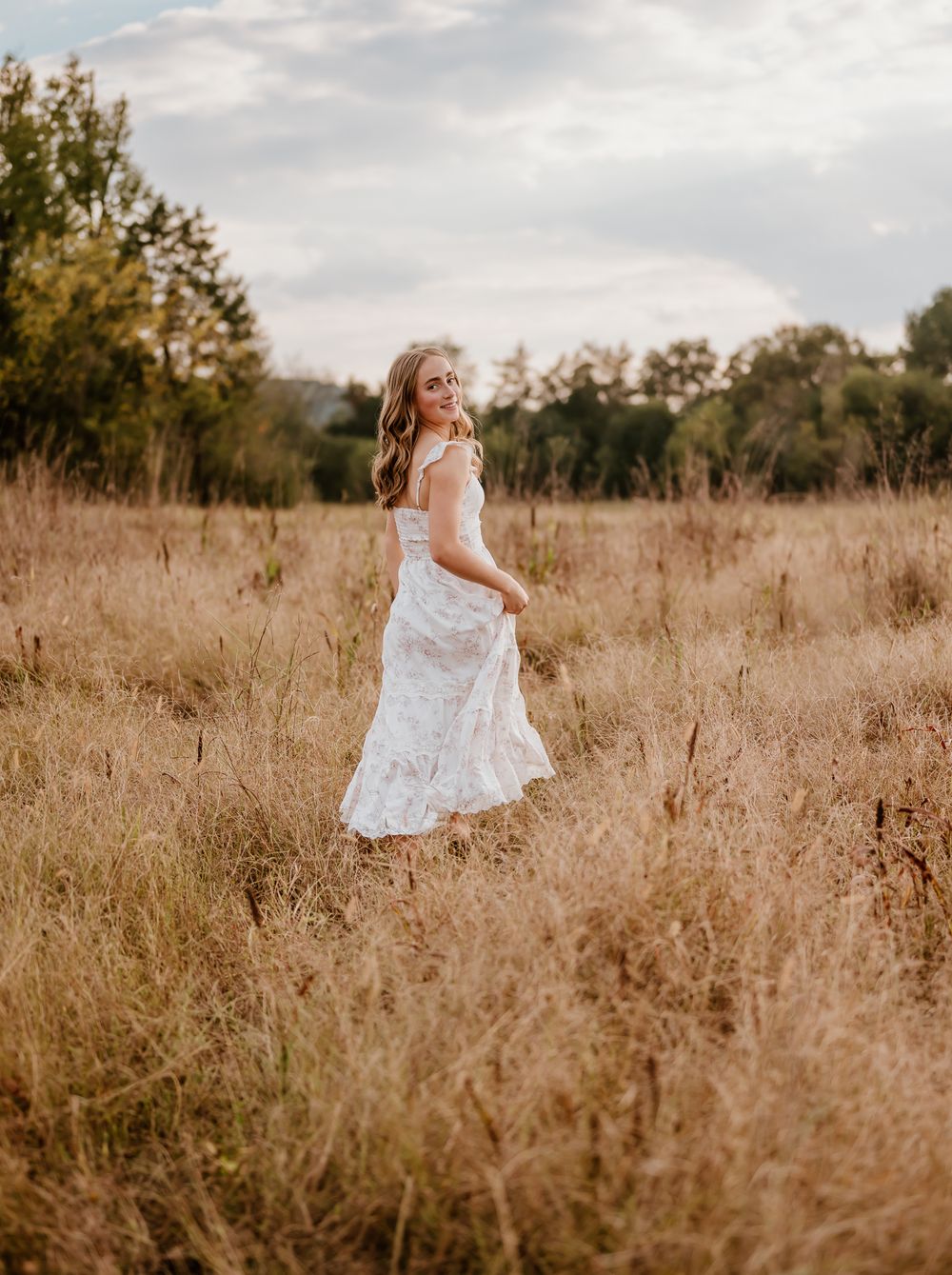 A figure in a flowing white dress twirls through a golden autumn field at sunset creating a dreamy ethereal scene.