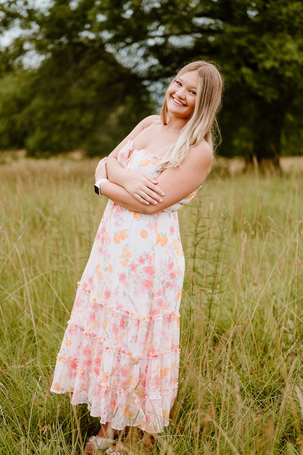 A woman stands in a flowing floral summer dress in a grassy field on a sunny day.