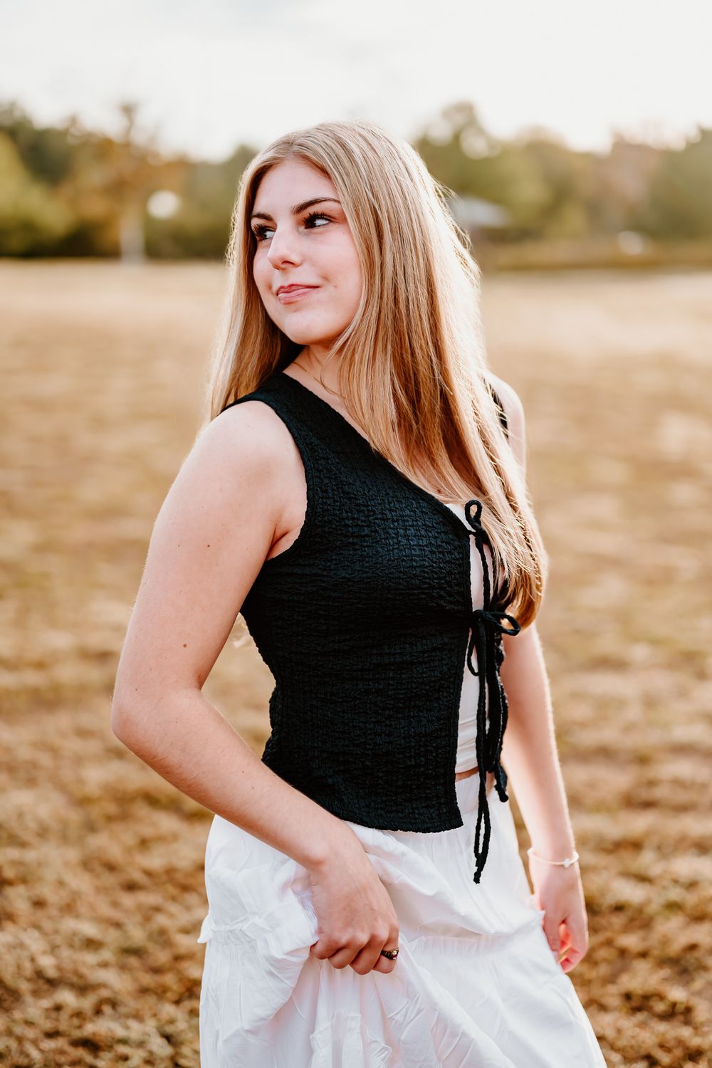 A person in a black top and white skirt poses gracefully in a sunlit field during golden hour.