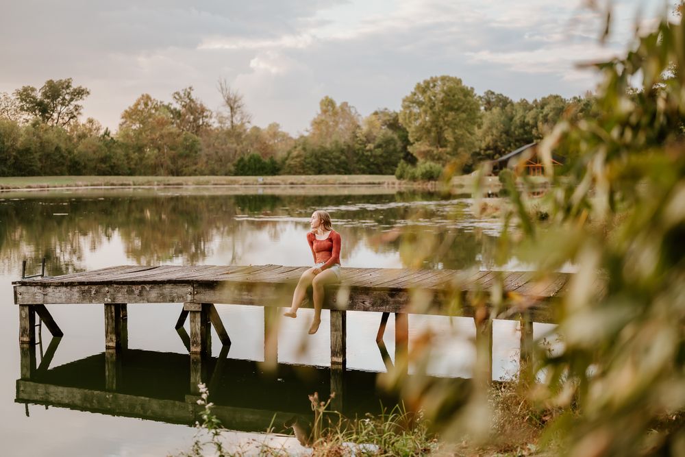 People sit together on a wooden dock overlooking a tranquil lake during golden hour.