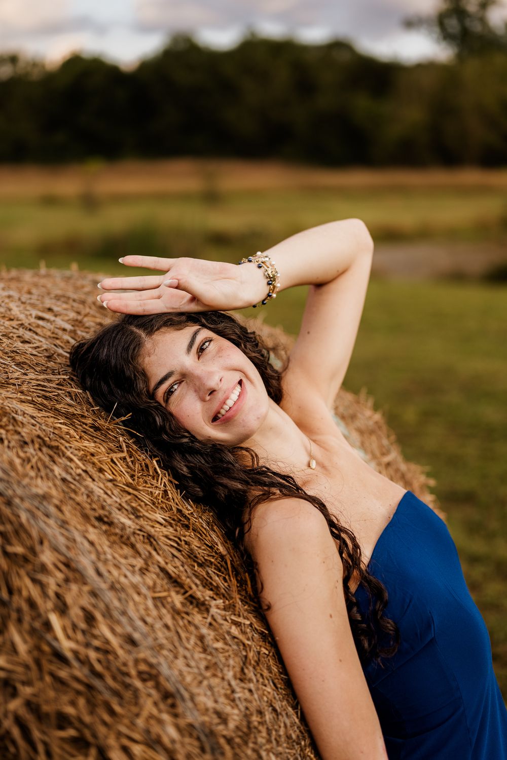 A woman in a navy blue dress poses gracefully against a rustic hay bale during golden hour.