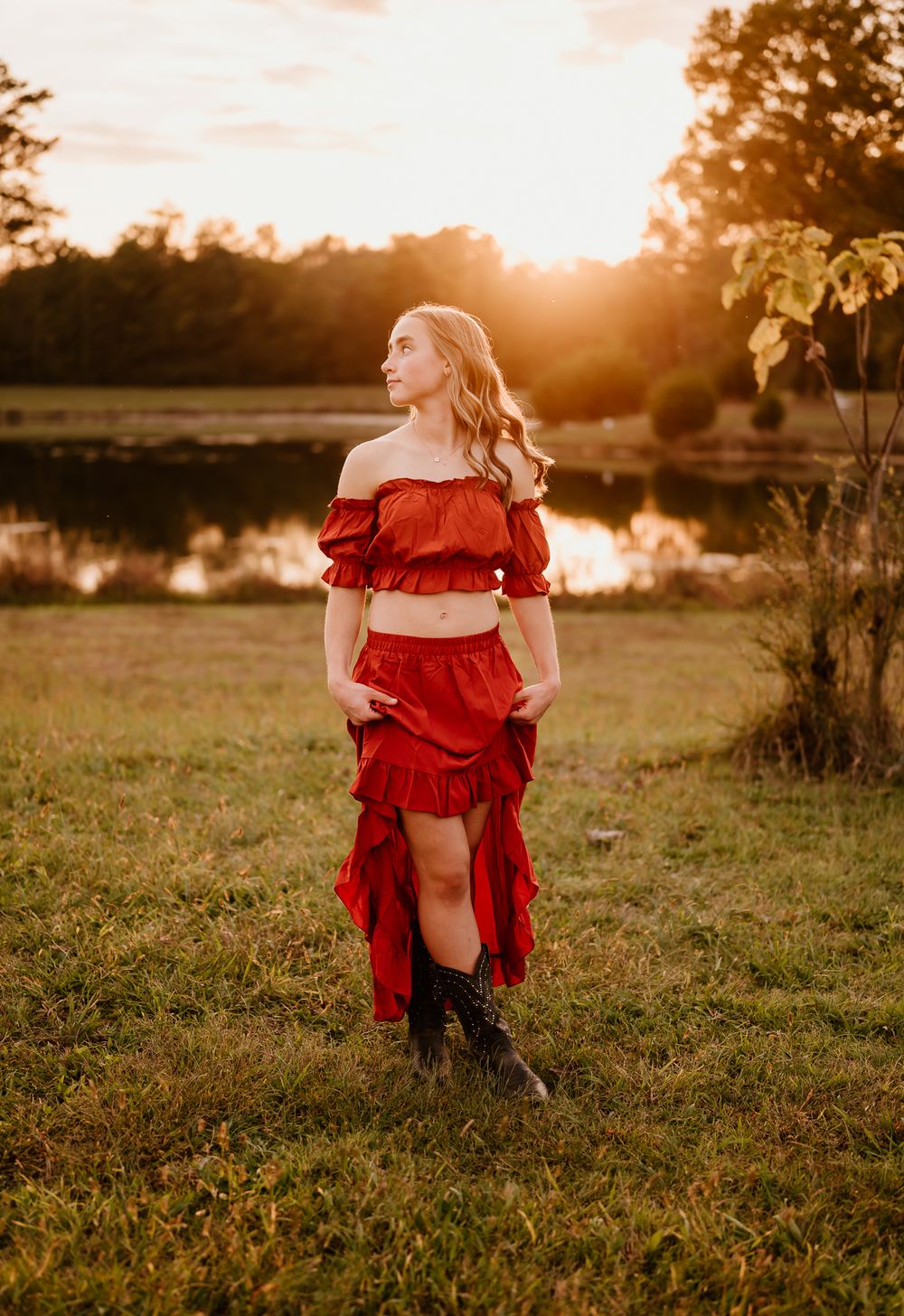 A person in a flowing red dress poses gracefully in a sunlit field during golden hour.