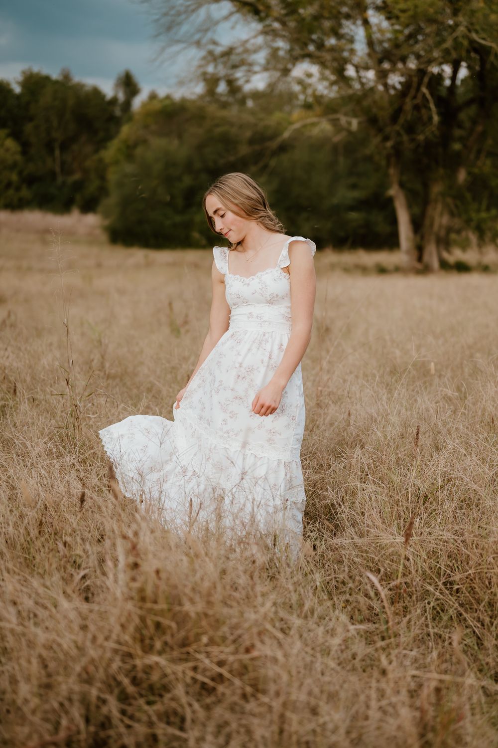 A woman in a white lace dress sits gracefully in a golden autumn field during a dreamy outdoor photoshoot.