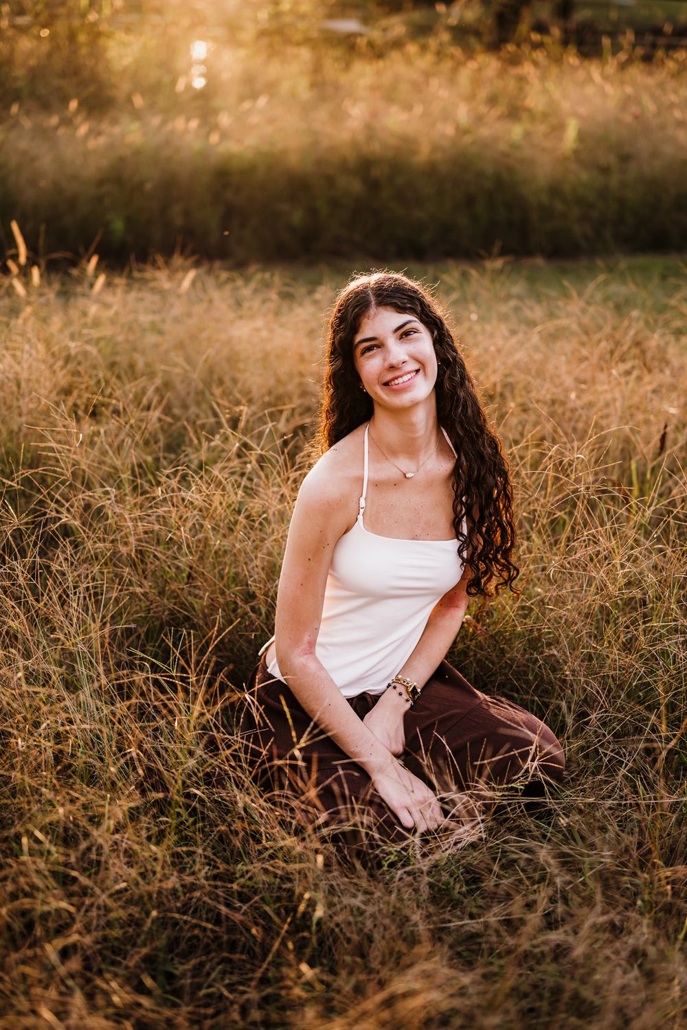 A person in a white top sits in golden grass during sunset creating a warm, dreamy outdoor portrait.