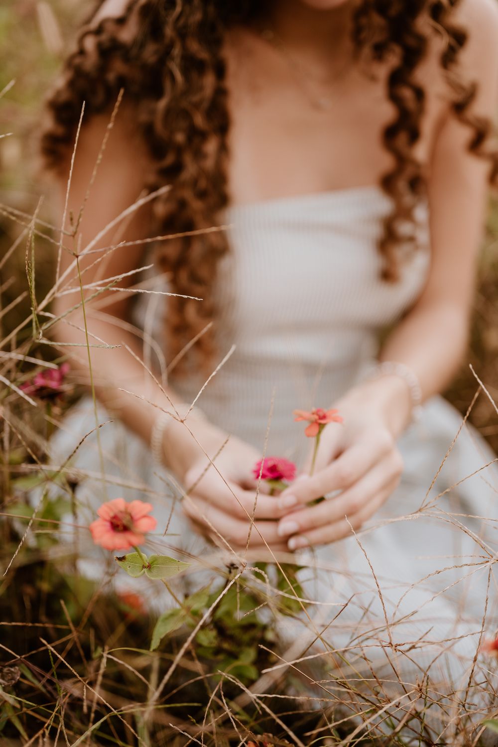 Hands gently reach towards delicate pink flowers blooming in a garden with soft natural lighting and bokeh effect.
