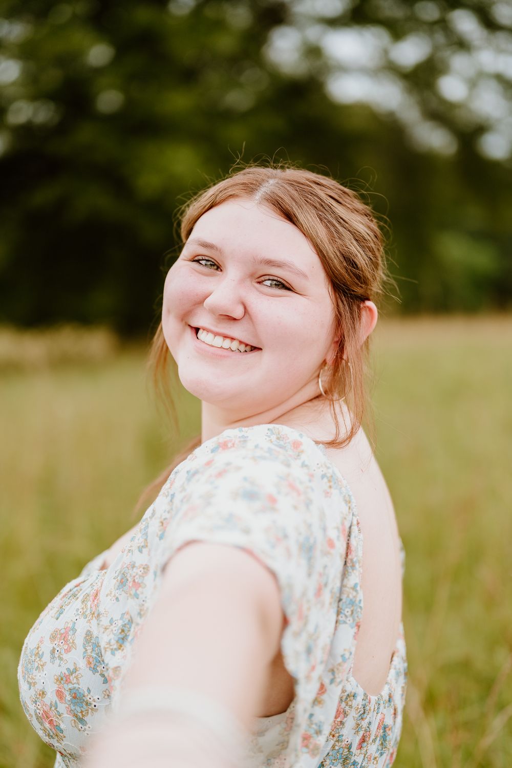 A joyful person in a floral dress poses in a sunny meadow during a summer photoshoot session.