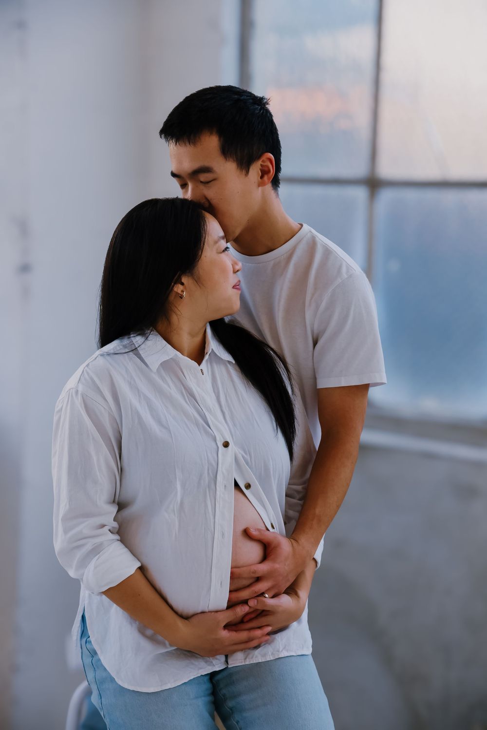 Couple in casual wear embracing near bright windows.
