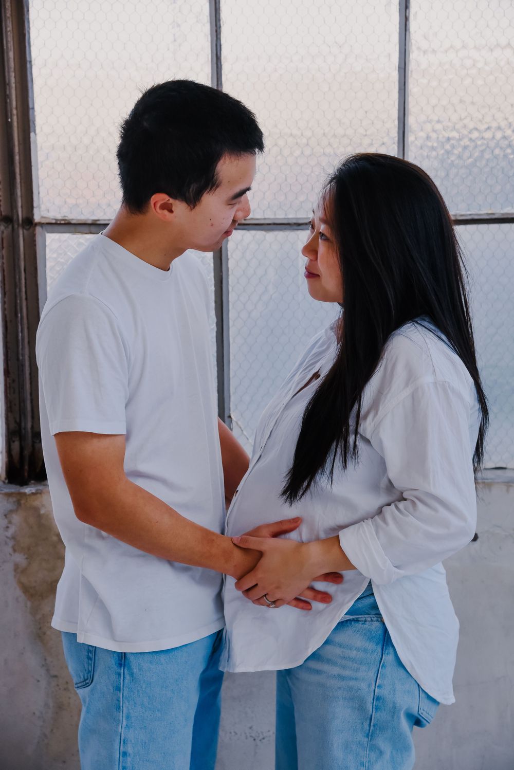 Couple in white tops and jeans sharing tender moment by window.