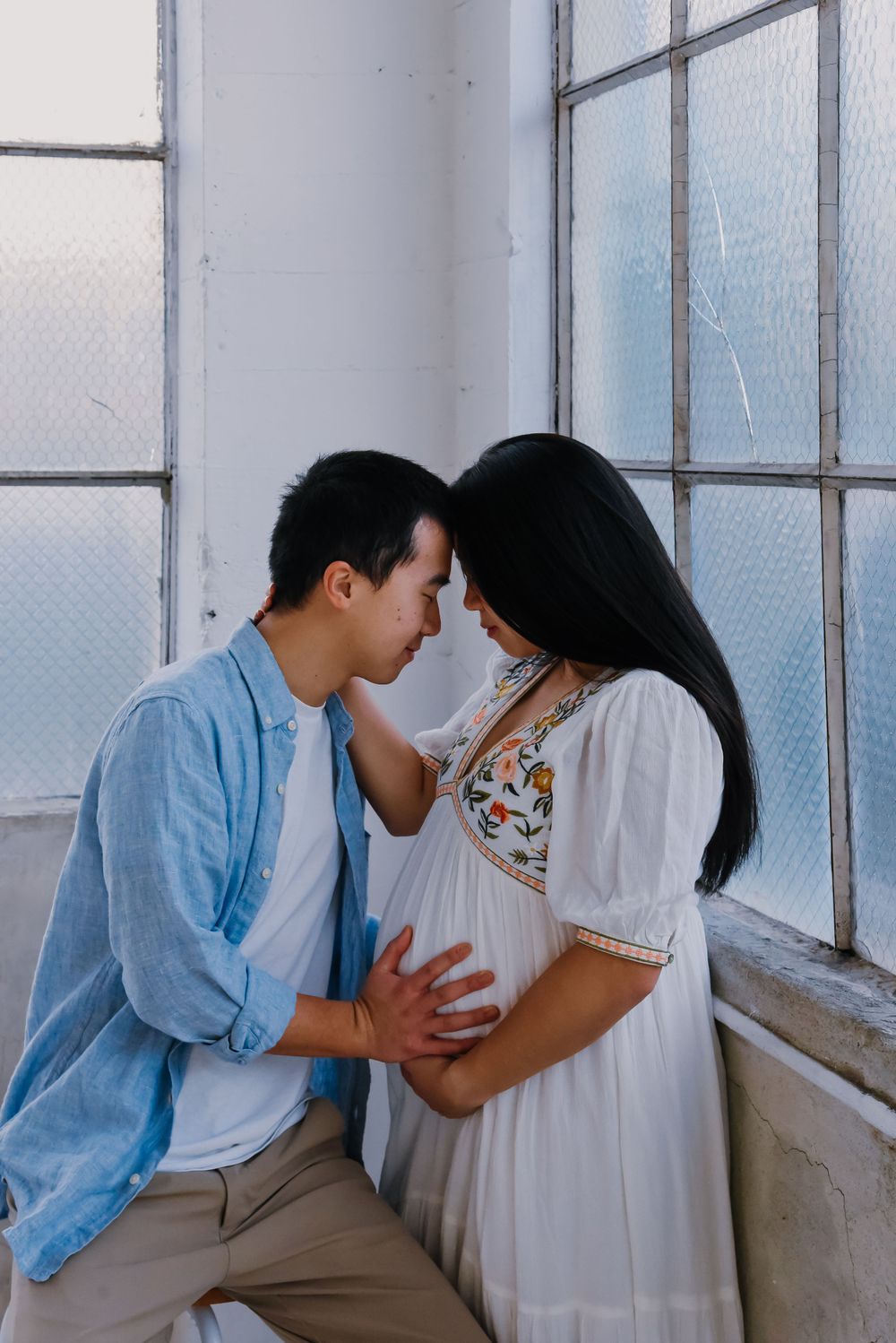 Intimate maternity photos with couple by bright window.