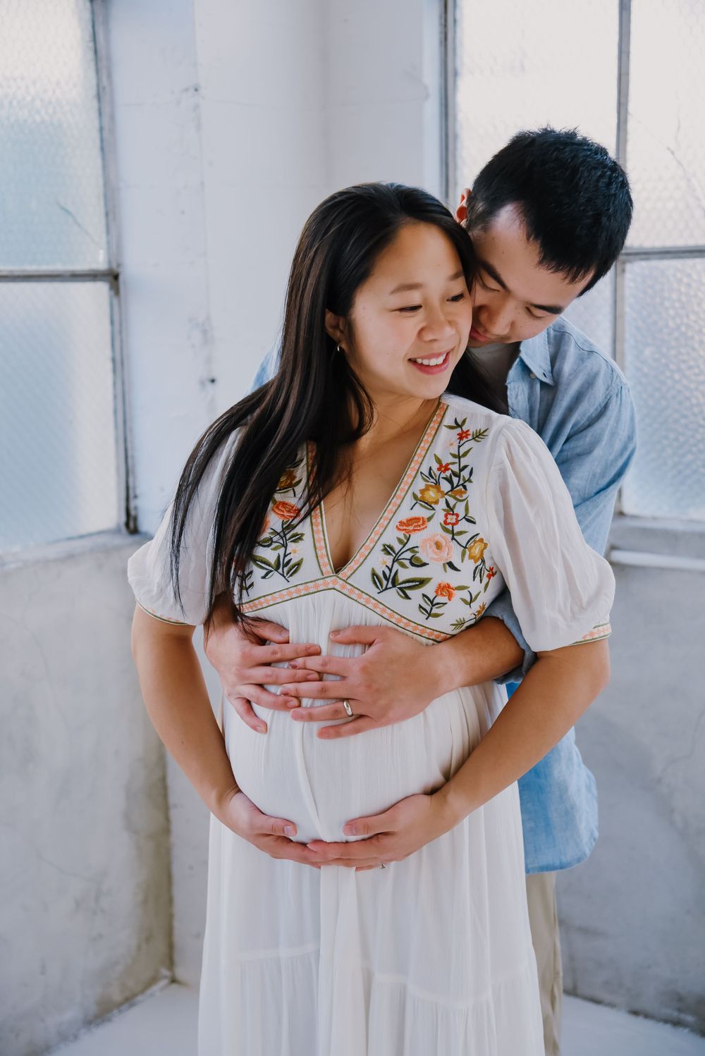 Intimate maternity photo of couple embracing near windows.