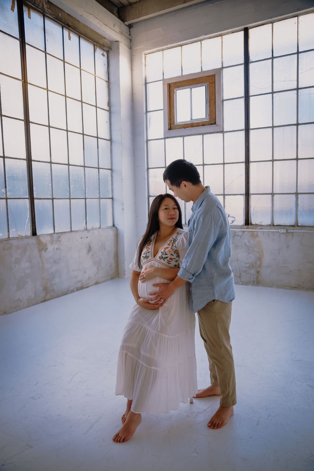 Couple poses for maternity photos in minimalist industrial setting.